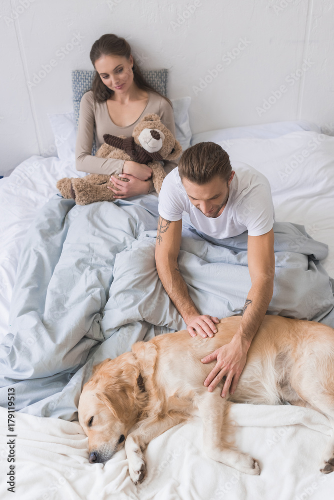 Couple in bed petting dog
