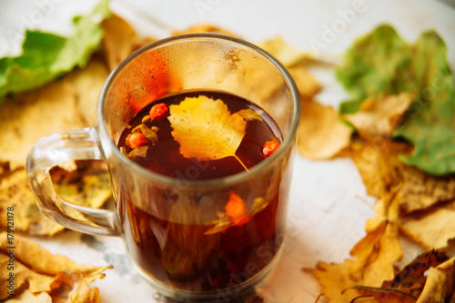 Autumn leaves and hot steaming cup of coffee. Wooden table on sun light background. Fall time concept.