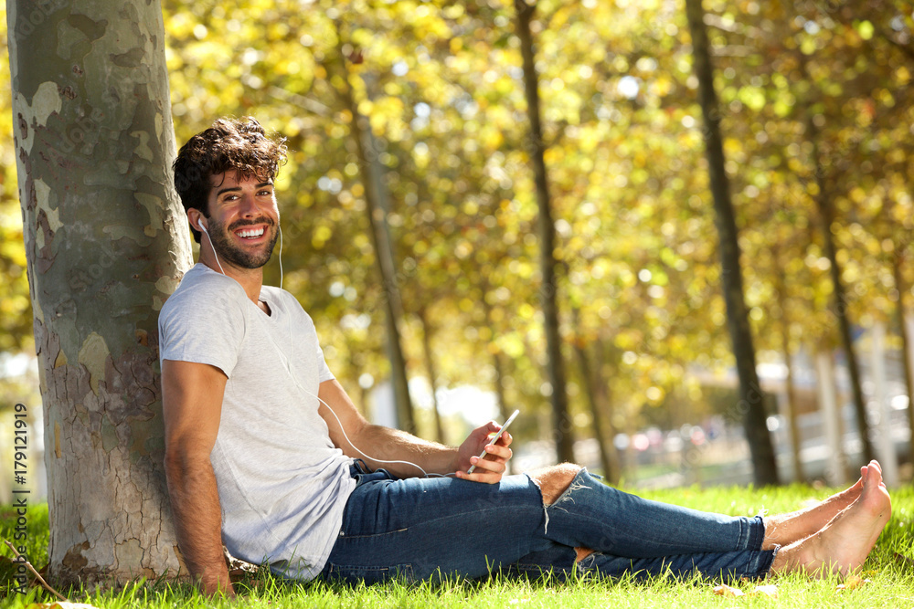 Happy man sitting in grass with cellphone and headphones Happy man sitting in grass with cellphone and headphones