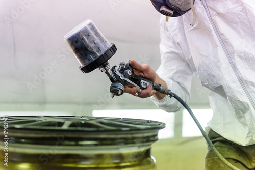 A varnisher is painting an alloy rim of a car with a spray gun. No face but dust mask photo