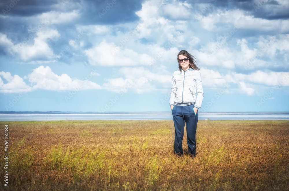 Young woman smiling in the midst of a orange lawn, she looks at the camera, so carefree. Steppe landscape. Baskunchak lake at background. Travel picture