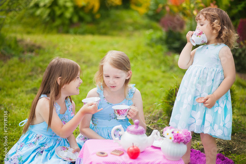 Three sisters playing tea party outdoors.