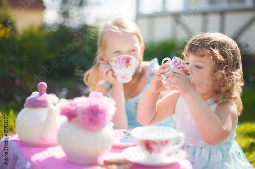 Two sisters playing tea party outdoors.