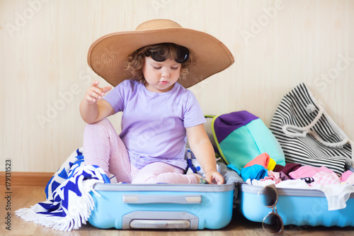 Little kid sitting inside a suitcase, ready for a big journey.