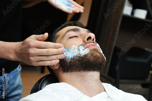 The hairdresser prepares the face for shaving and smears the face with foam
