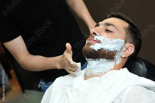 Фотография Barber preparing man face for shaving with hot towel on face in barber shop