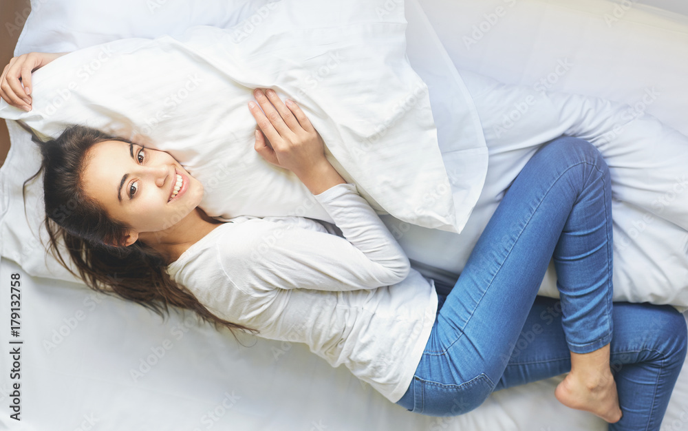 young smiling woman lying on bed hugging pillow young smiling woman lying on bed hugging pillow