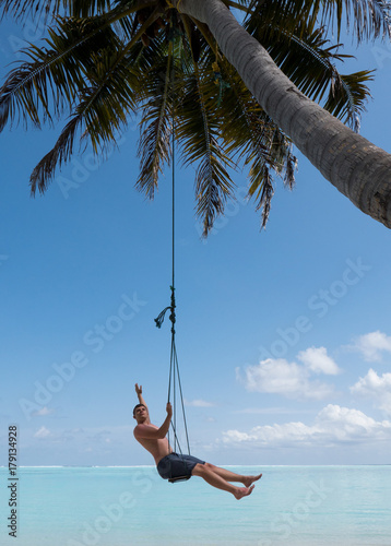 Outdoor summer vacation tropic palm style portrait of young strong man on beach swing blue water and sky. Single man alone while swinging on the beach at Maldives Island.Indian ocean vacation holidays