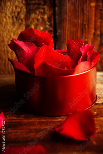Many rose petals inside open gift box and scattered on old vintage wooden plates. Sweet holiday background with rose petals. photo