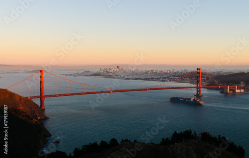 Container ship passing under the Golden Gate bridge at sunset portraying the importation of everything from China