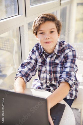 Teen boy using laptop by wi...