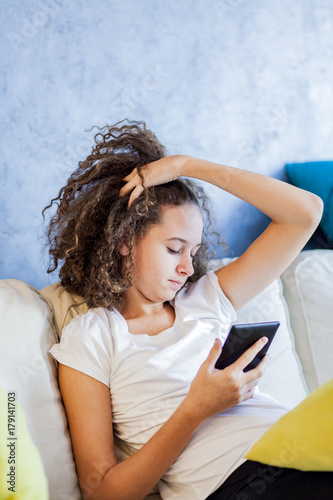Teen girl resting and usiing digital tablet on sofa at home