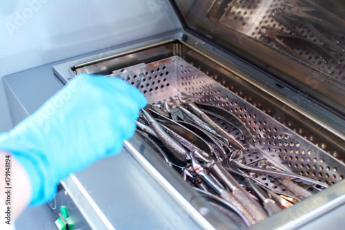 Close up of dentist's hands taking out sterilizing medical instruments from autoclave.