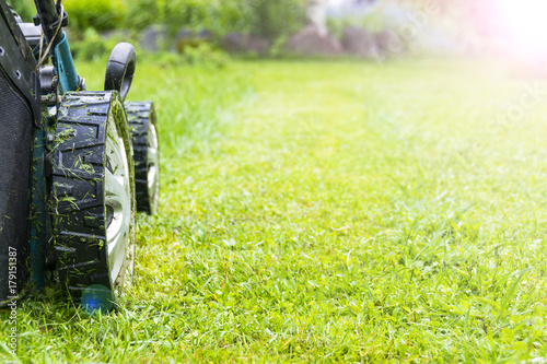 Fotografie Mowing lawns, Lawn mower on green grass, mower grass equipment, mowing gardener care work tool, close up view, sunny day