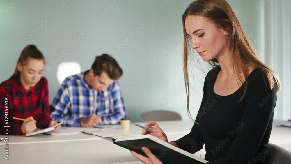 Portrait of a young female student reading a book and working on her homework while her friends are studying on the background. Slowmotion shot Portrait of a young female student reading a book and working on her homework while her friends are studying on the background. Slowmotion shot