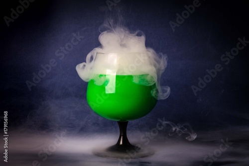 Smoke into cocktail glass on a black background. Witch potion background for Halloween. Unusual bar drink.