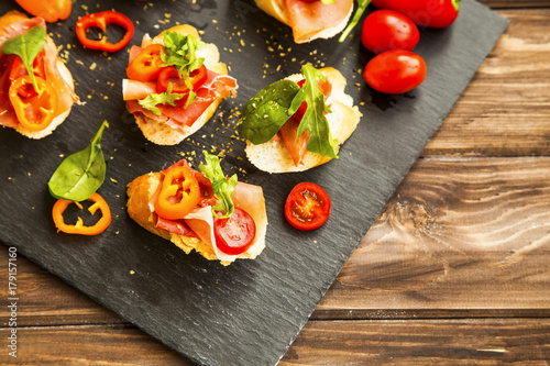 Canapes appetizer with prosciutto ham, pepper slices, tomatoes and green spinach and rucola leaves, healthy crostini or bruschettas italian appetizer seasoned