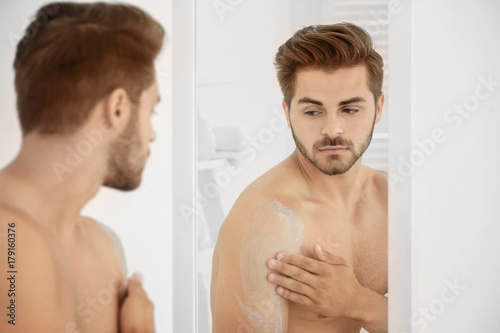 Young man applying cream on...
