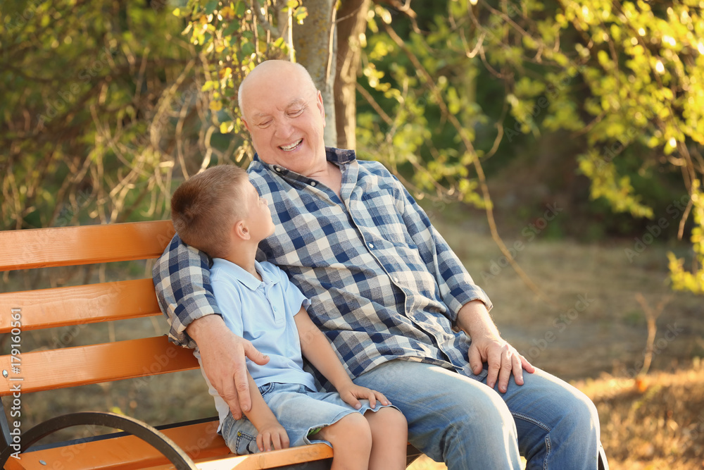 Happy senior man with grandson sitting on bench in park