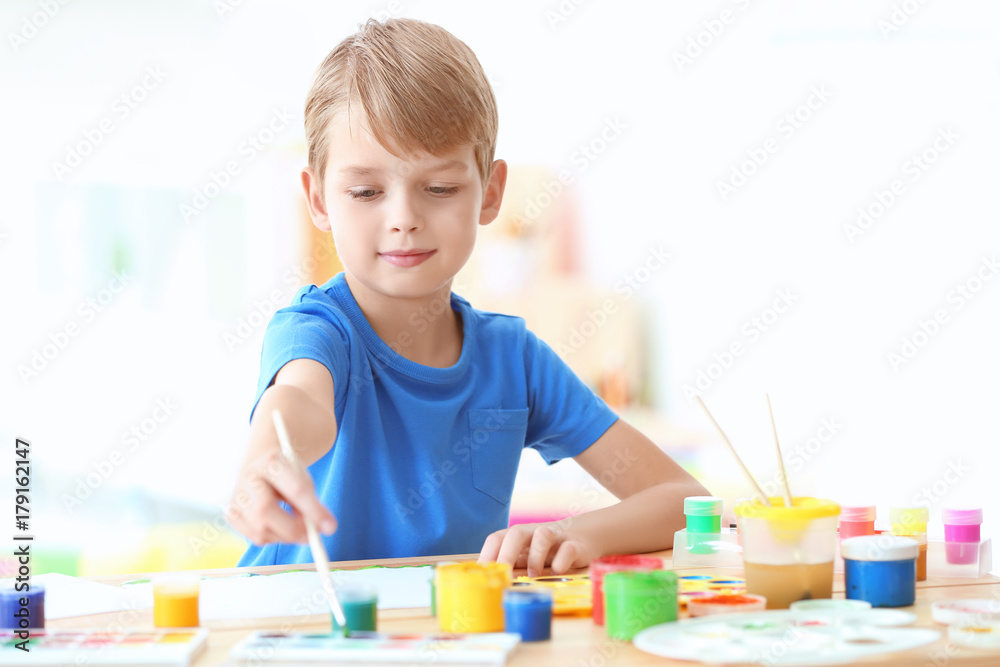 Cute boy painting picture at table indoors Cute boy painting picture at table indoors