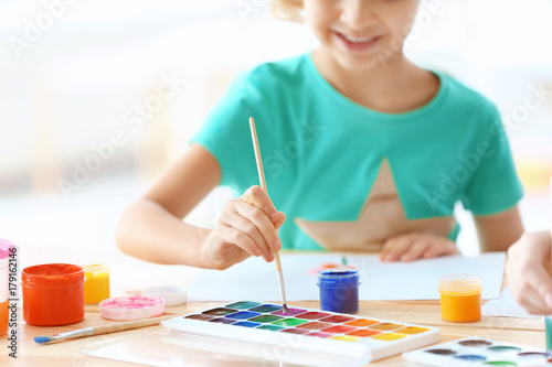 Cute girl painting picture at table indoors
