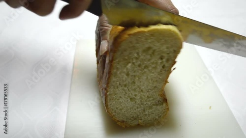 A Loaf of Bread Cut With a Knife/ Women`s hands cut a loaf of white bread into pieces. Closeup of hands cutting a white bread into pieces
