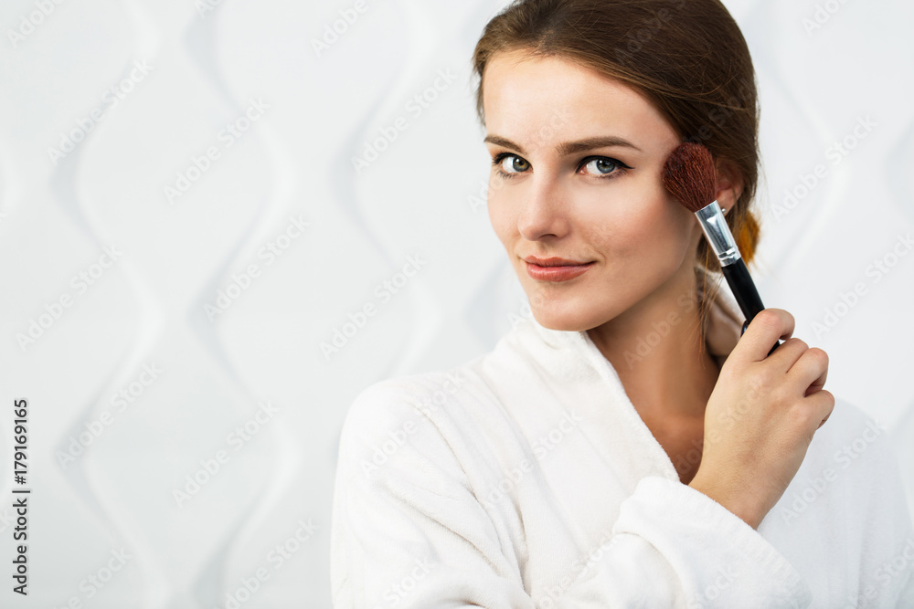 Lovely girl in the white bathrobe using makeup brush in the white background Lovely girl in the white bathrobe using makeup brush in the white background
