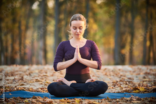 Beautiful young woman meditates in yoga asana Padmasana - Lotus pose on the wooden deck in the autumn park. photo