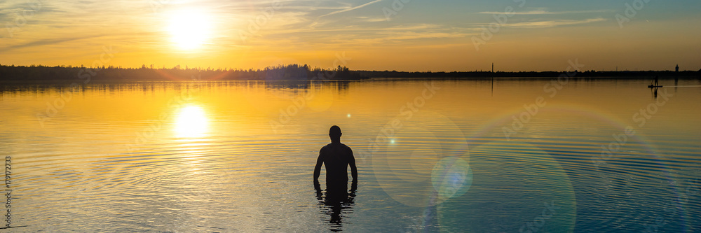 Panorama of a men going into a lake at beautiful sunset