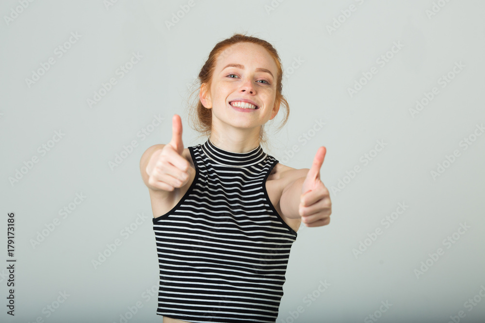 beautiful young smiling girl with red hair with an approving gesture of hands on a light background beautiful young smiling girl with red hair with an approving gesture of hands on a light background