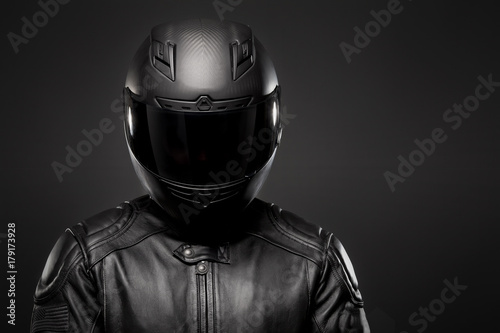 Man wearing a black leather motorcycle jacket and helmet on dark background. photo