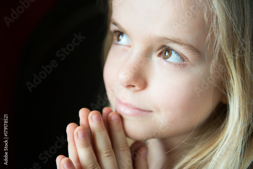 Portrait of a a little girl, with clasped hand, in act of prayer. Black background.