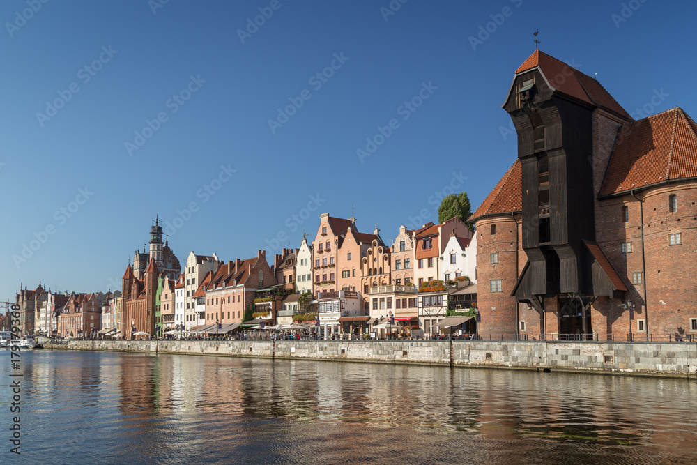 View of the Crane and other old buildings along the Long Bridge waterfront and their reflections on the Motlawa river at the Main Town in Gdansk, Poland, in the daytime.