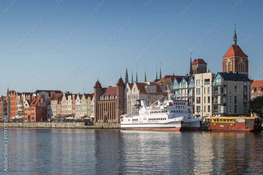 View of two boats and old buildings at the Long Bridge waterfront at the Main Town in Gdansk, Poland, on a sunny day.