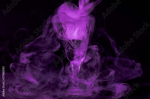 Smoke into cocktail glass on a black background. Witch potion background for Halloween. Unusual bar drink.