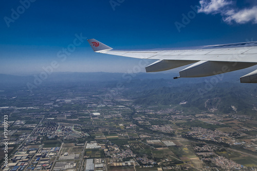 An aerial picture of beautiful mountains and urban houses taken mid-flight from the airplane window with the wing of the plane visible.