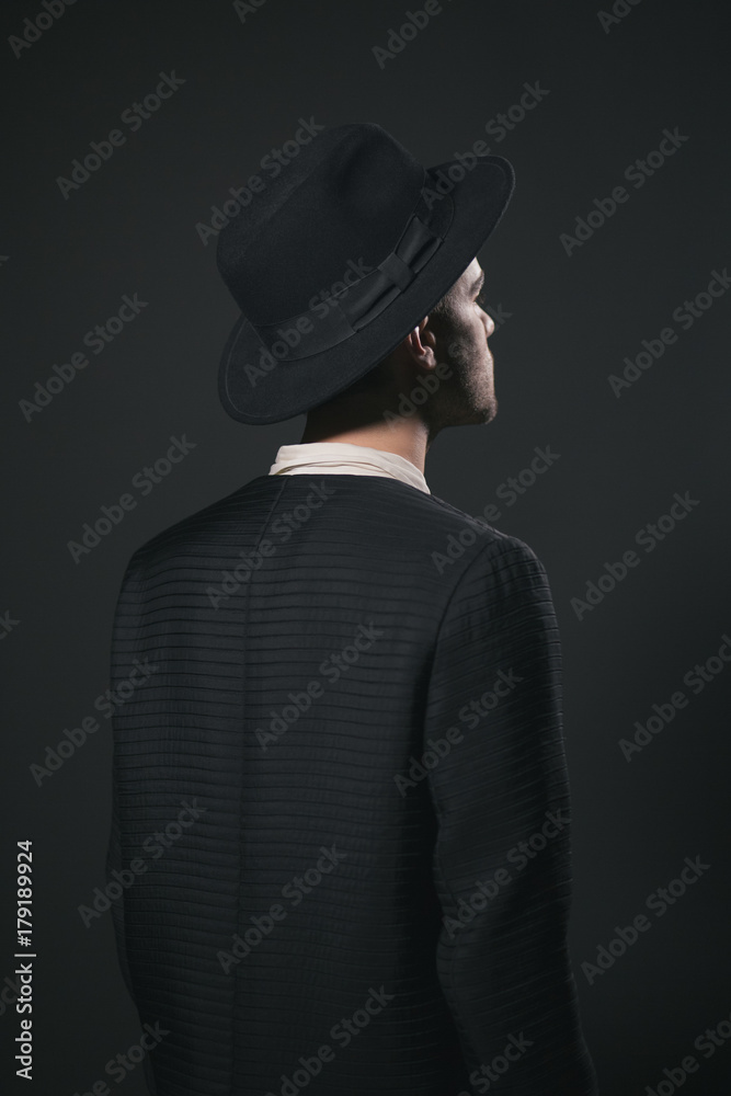 Dark portrait of the back of the man, wearing a hat against a black backgorund Dark portrait of the back of the man, wearing a hat against a black backgorund