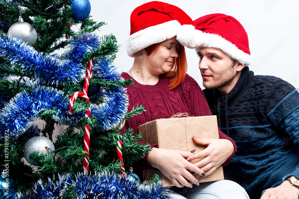 Spirit of Christmas and new year. Concept of a holiday and days off. A loving couple in Santa Claus hats. The girl and her boyfriend enjoy the holiday and gifts Spirit of Christmas and new year. Concept of a holiday and days off. A loving couple in Santa Claus hats. The girl and her boyfriend enjoy the holiday and gifts