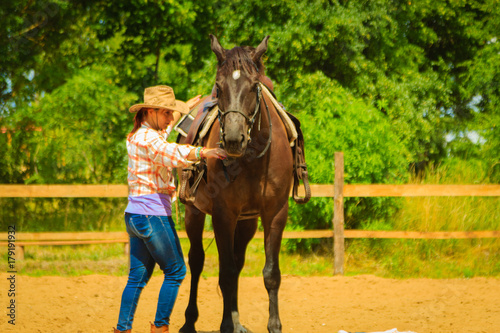 Cowgirl getting horse ready for ride on countryside