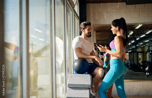 Shape sporty beautiful girl flirting with a muscular guy next to her while standing near the window in the gym.