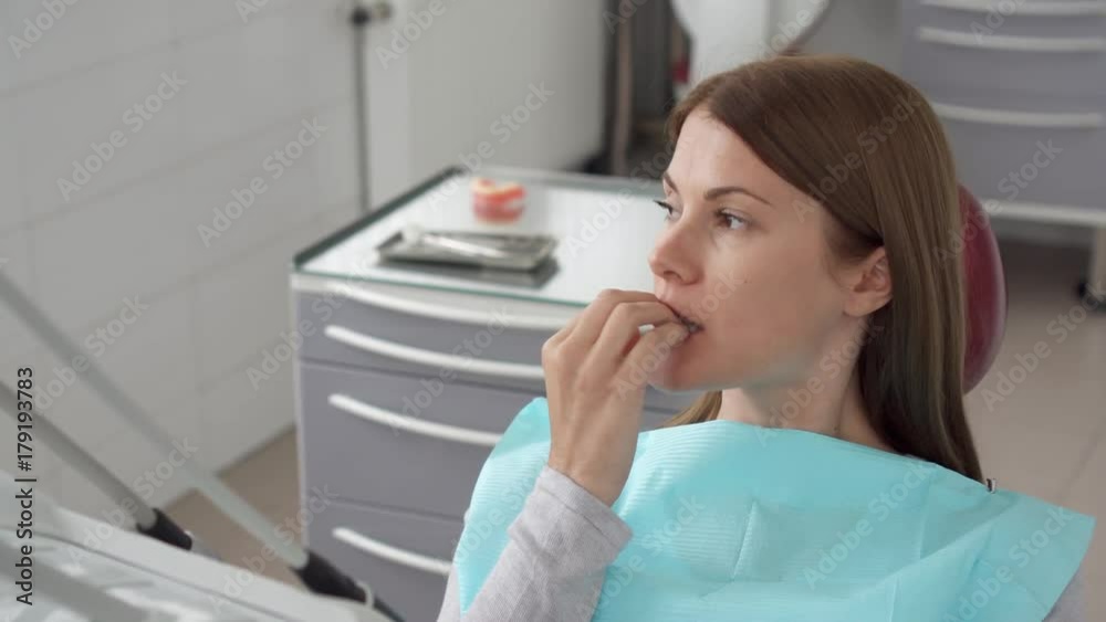 Woman patient in dental clinic. Waiting in dental chair for professional doctor stomatologist. Anxious, afraid, biting her nails. Dental equipment on background. Dental check up Woman patient in dental clinic. Waiting in dental chair for professional doctor stomatologist. Anxious, afraid, biting her nails. Dental equipment on background. Dental check up