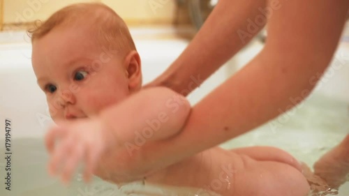 happy smiling glad baby boy bathing mother help enjoying bath healthy strong body surprised emotional face big eyes cute beautiful child tub bathroom healthcare pink gentle clean skin naked wet body photo