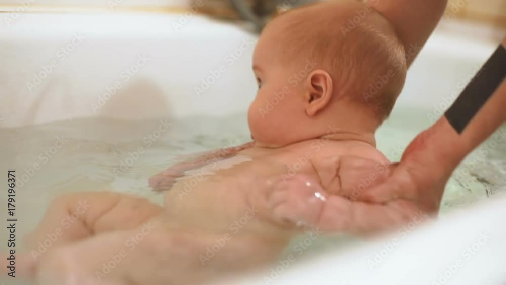 little kid bathing mother hands support clean body skin care healthy concept babyboy washing taking bath water tub home beauty human parenting glad infant adorable child calm interested newborn fun