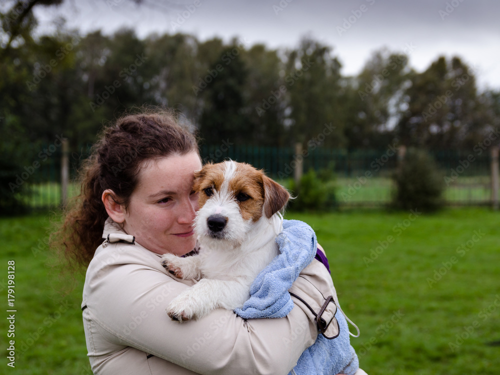 Szczeniak Jack Russell terrier na rękach swojej właścicielki. Zdjęcie w plenerze w wietrzny deszczowy jesienny dzień. Szczeniak Jack Russell terrier na rękach swojej właścicielki. Zdjęcie w plenerze w wietrzny deszczowy jesienny dzień.