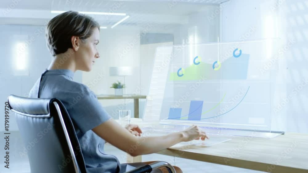 In the Near Future Beautiful Renewable Energy Scientist Works with Touchscreen Keyboard and Transparent Computer Display. Screen Shows Interactive User Interface with Flowing Pie Charts, Graphs. In the Near Future Beautiful Renewable Energy Scientist Works with Touchscreen Keyboard and Transparent Computer Display. Screen Shows Interactive User Interface with Flowing Pie Charts, Graphs.