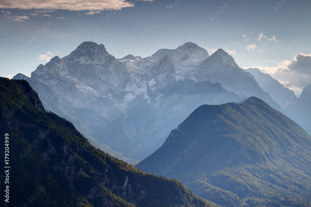 Triglav, highest peak of Slovenia, from the north with snowy Rjavina and Cmir peaks, green forests of Jerebikovec and deep Kot Valley in afternoon sun light, Triglav National Park, Julian Alps, Europe