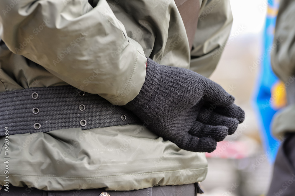 A person holds their gloved hand behind their back as they wear a paramilitary uniform