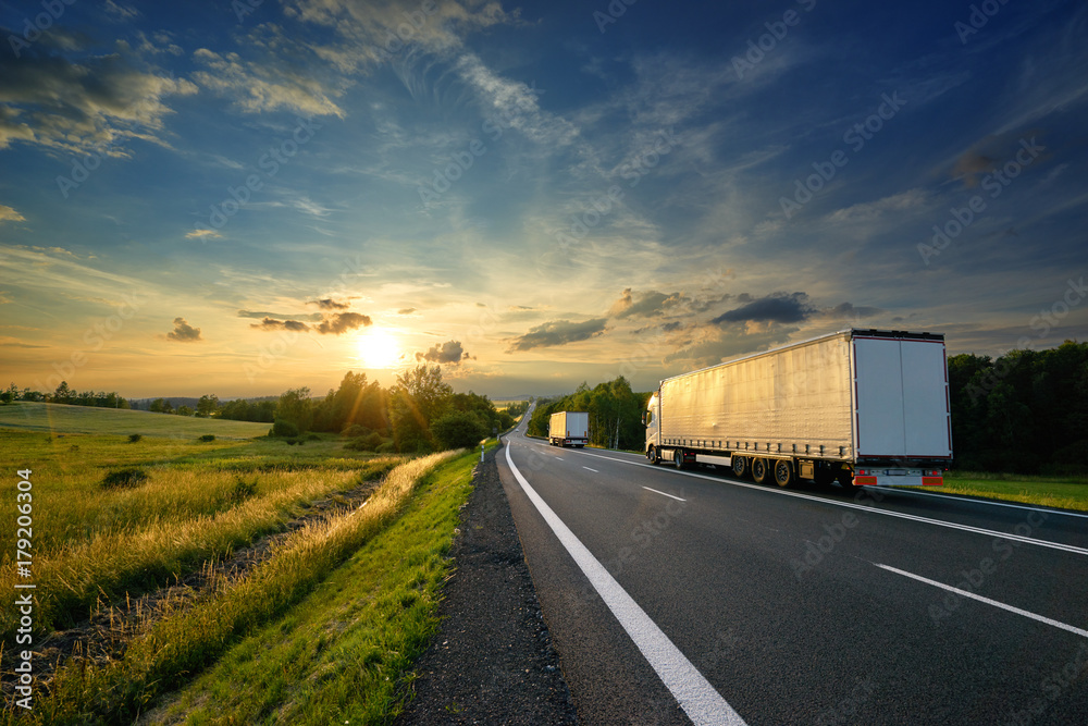 Trucks driving towards the setting sun on the road in rural countryside