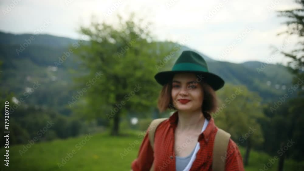 Tourist young woman wearing hat walking on the mountain. Active healthy hipster girl hiking in forest, traveler with backpack walking on path in the mountains Tourist young woman wearing hat walking on the mountain. Active healthy hipster girl hiking in forest, traveler with backpack walking on path in the mountains