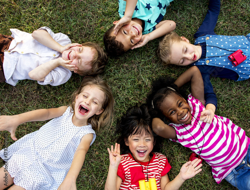 Group of kindergarten kids lying on the grass at park and relax with smiling